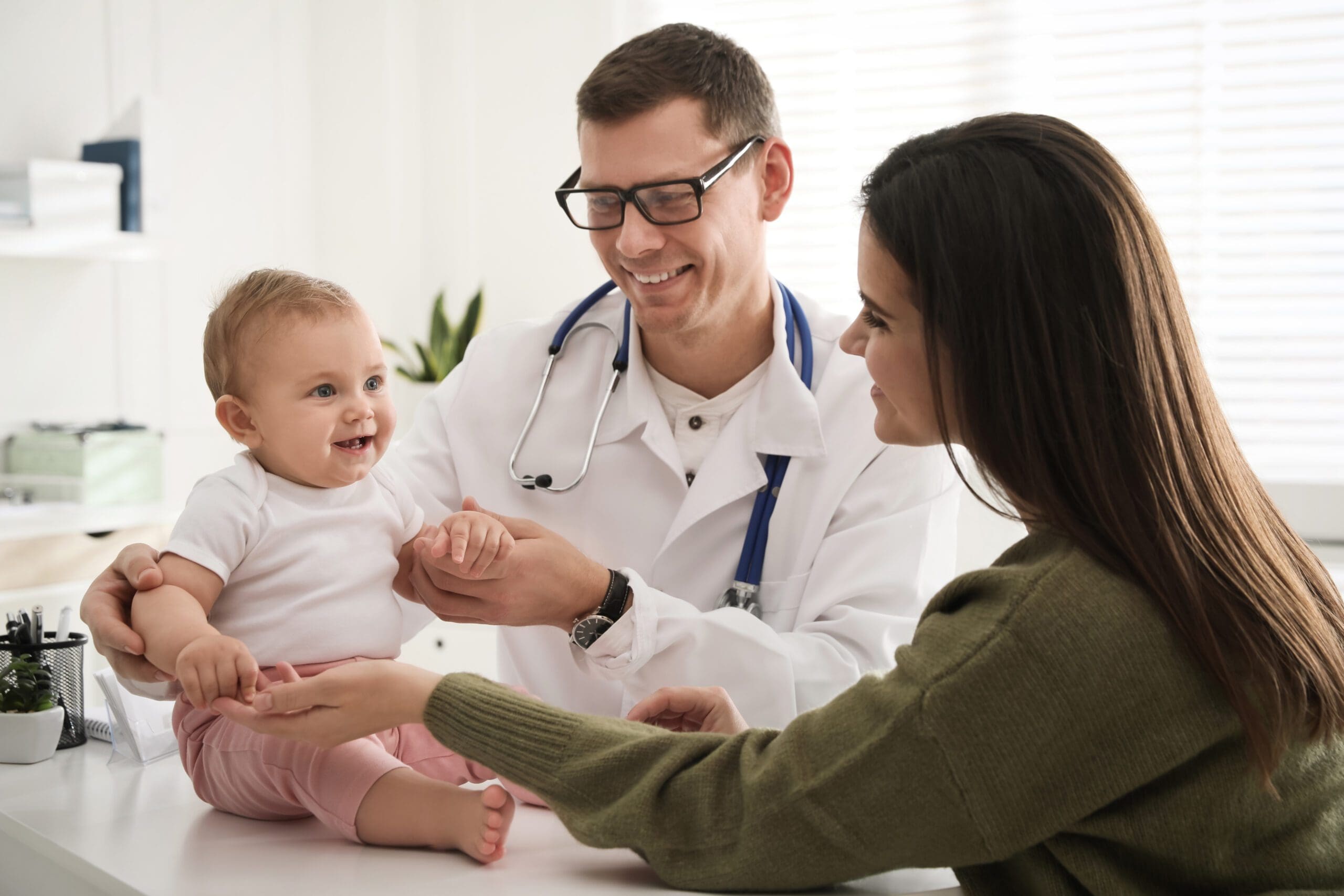 Doctor examining a smiling baby with mother.