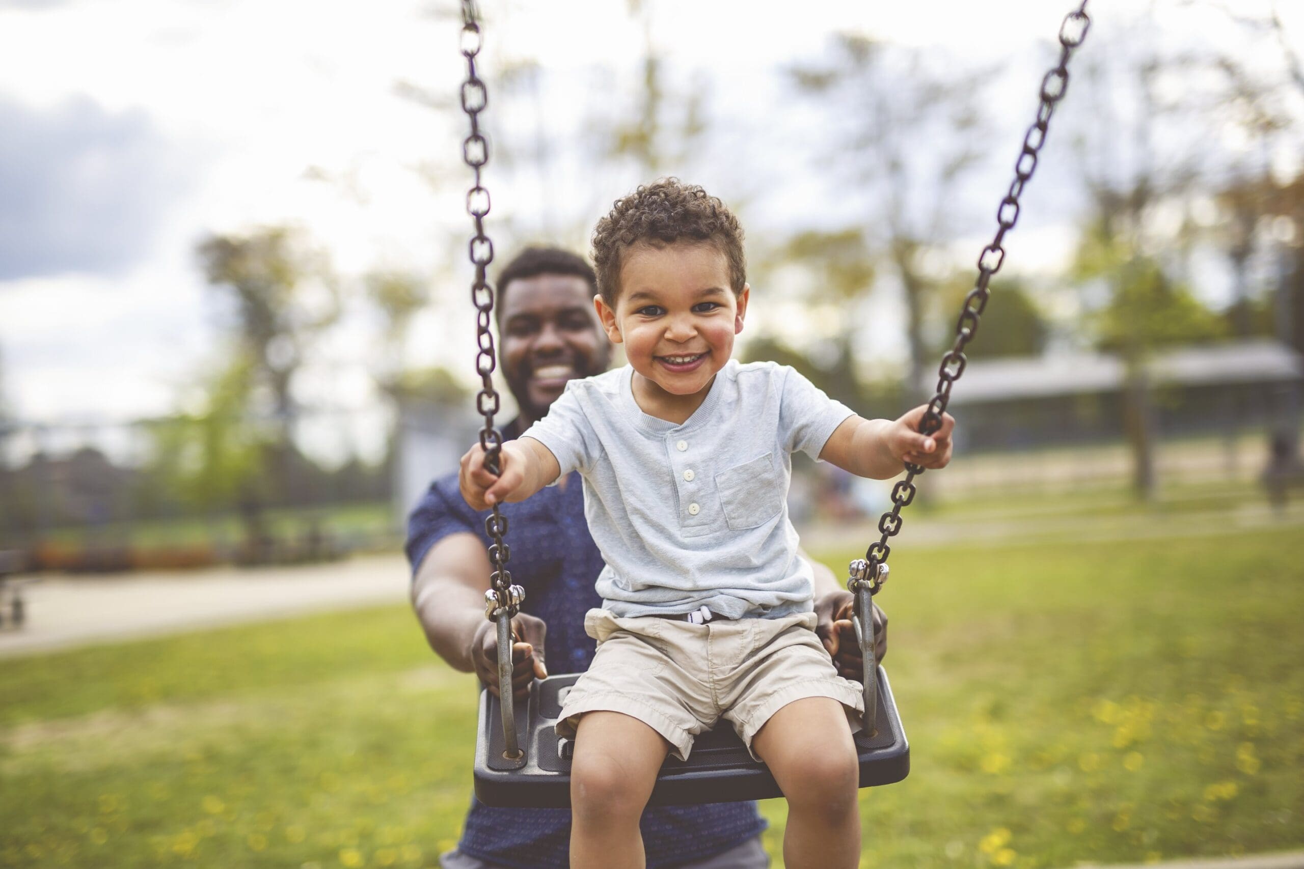 Child on swing with adult in park.